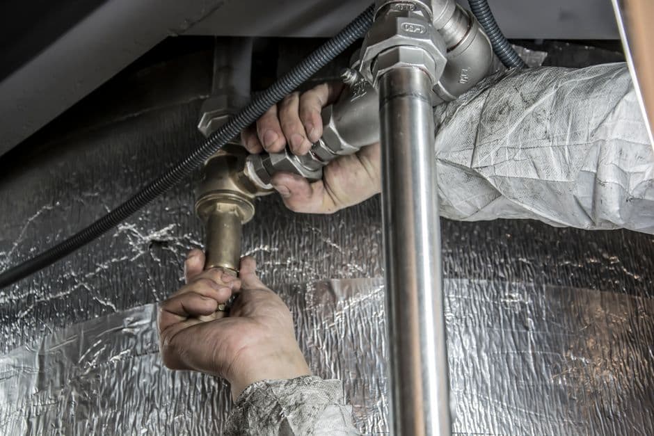 A plumber fitting a pipe under a sink